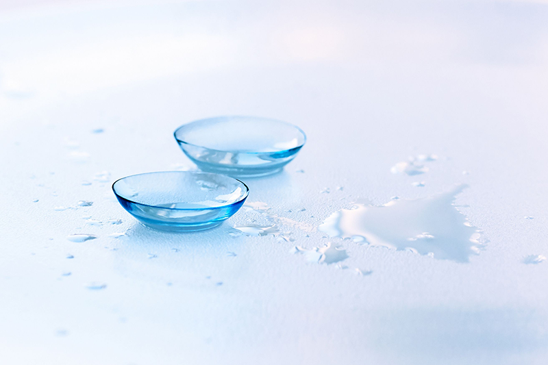 Contact lenses and water drops on a light blue background.